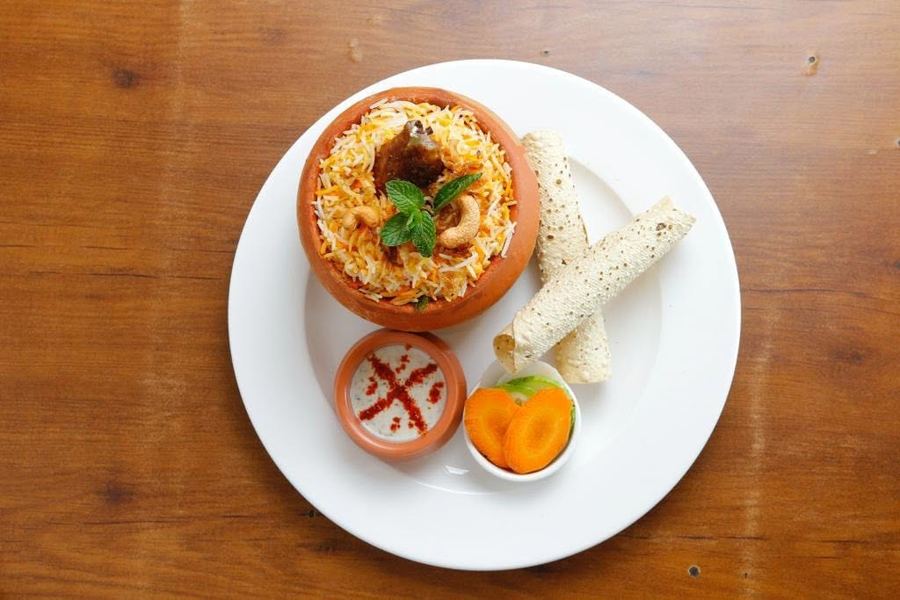 Matka biryani plated with raita and papad