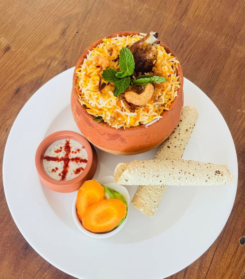 Matka mutton biryani served in a clay pot with raita and papad