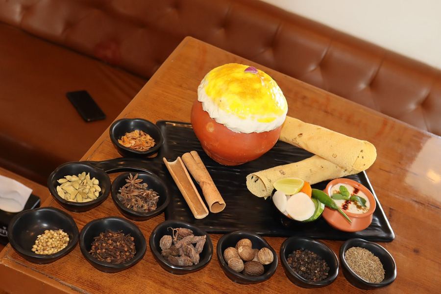 Whole spices laid out beside a sealed matka biryani